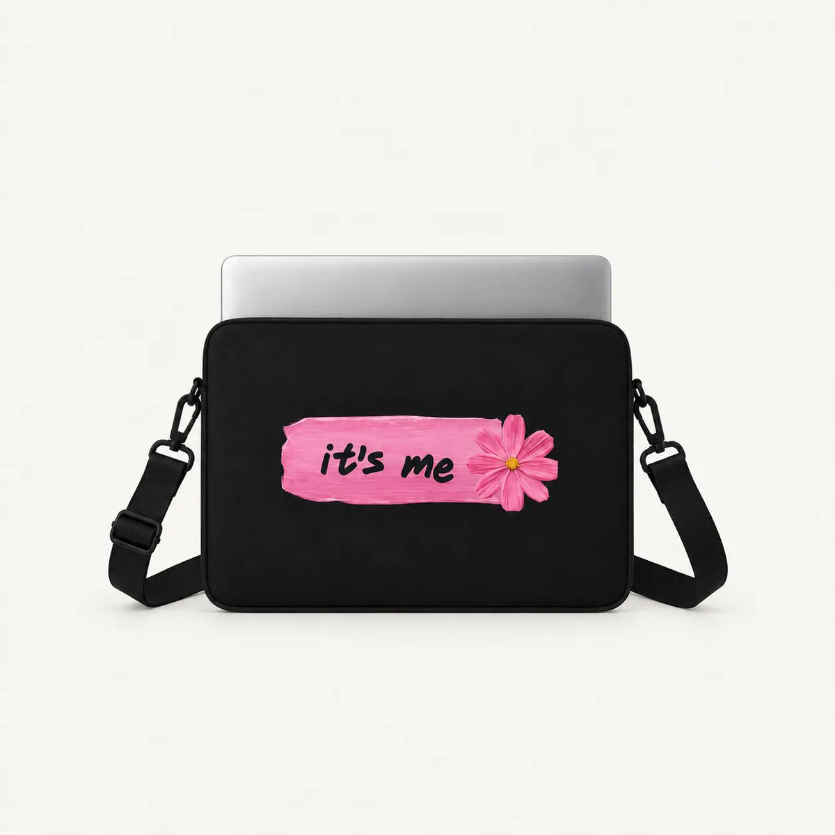 A black laptop sleeve with a pink brush-stroke style graphic that reads 'it's me' in black script next to a pink flower, shown with a silver laptop on a white background.
