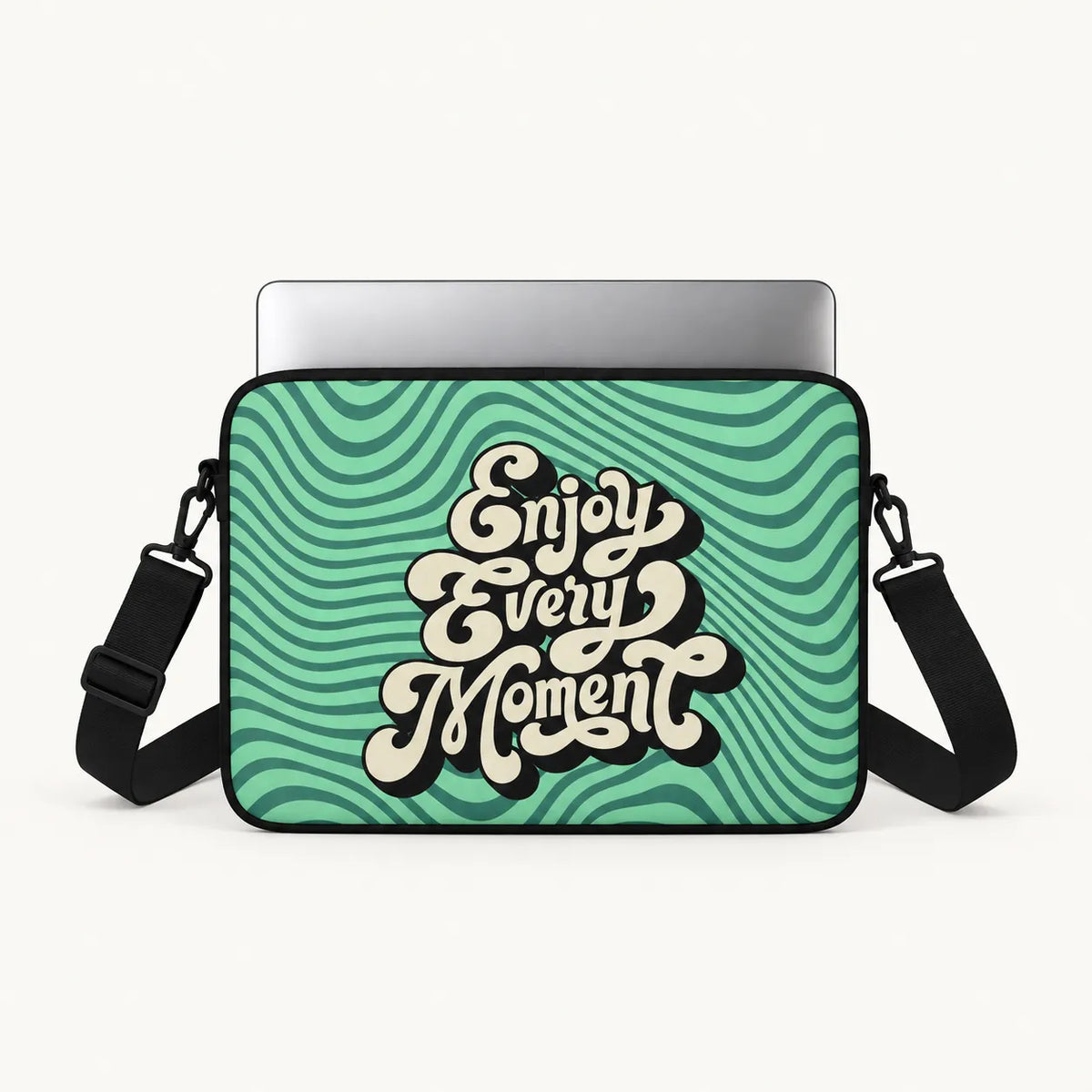A laptop sleeve with a green wavy pattern and the phrase 'Enjoy Every Moment' in cream bubble lettering, shown on a light gray background with a silver laptop partially inserted.
