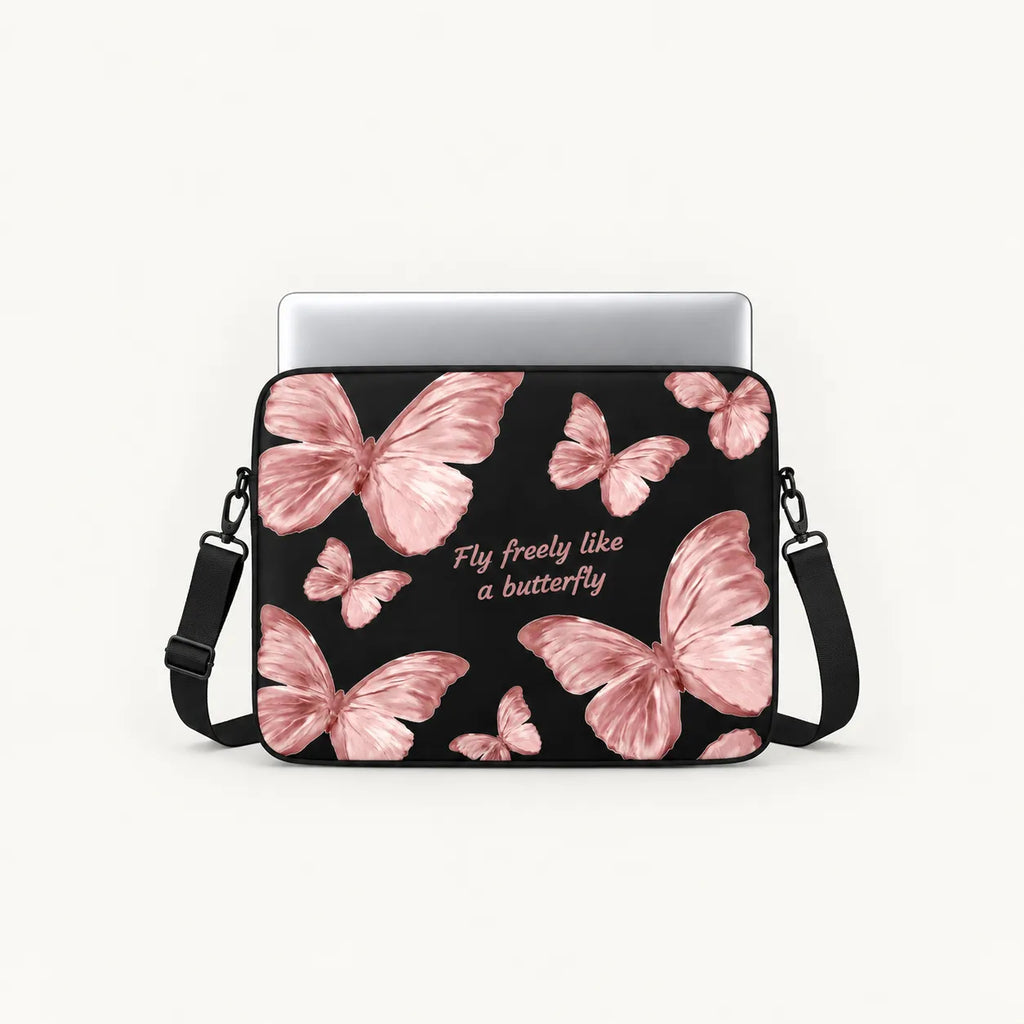 A black crossbody laptop bag with a pink butterfly pattern and the text 'Fly freely like a butterfly' in white script, shown with a silver laptop inserted on a light gray background.