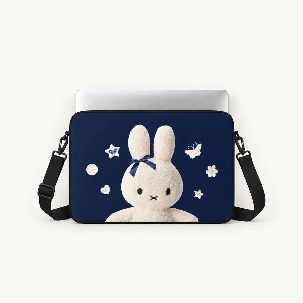 A navy blue laptop sleeve featuring a cute white bunny illustration with a blue bow, surrounded by white stars and flowers, shown with a silver laptop and black shoulder strap on a light background.