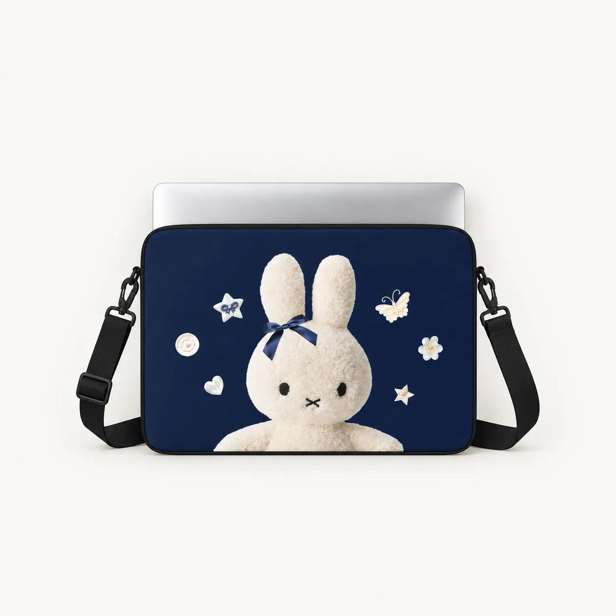 A navy blue laptop sleeve featuring a cute white bunny illustration with a blue bow, surrounded by white stars and flowers, shown with a silver laptop and black shoulder strap on a light background.