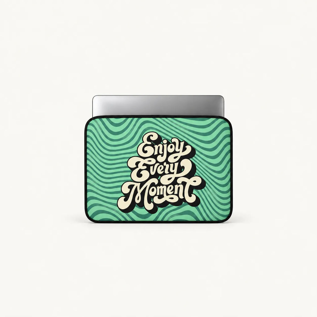A laptop sleeve featuring a retro wavy green and teal pattern with the phrase 'Enjoy Every Moment' in stylized cream lettering, shown on a light gray background.
