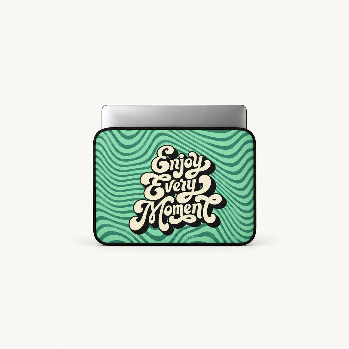A laptop sleeve featuring a retro wavy green and teal pattern with the phrase 'Enjoy Every Moment' in stylized cream lettering, shown on a light gray background.