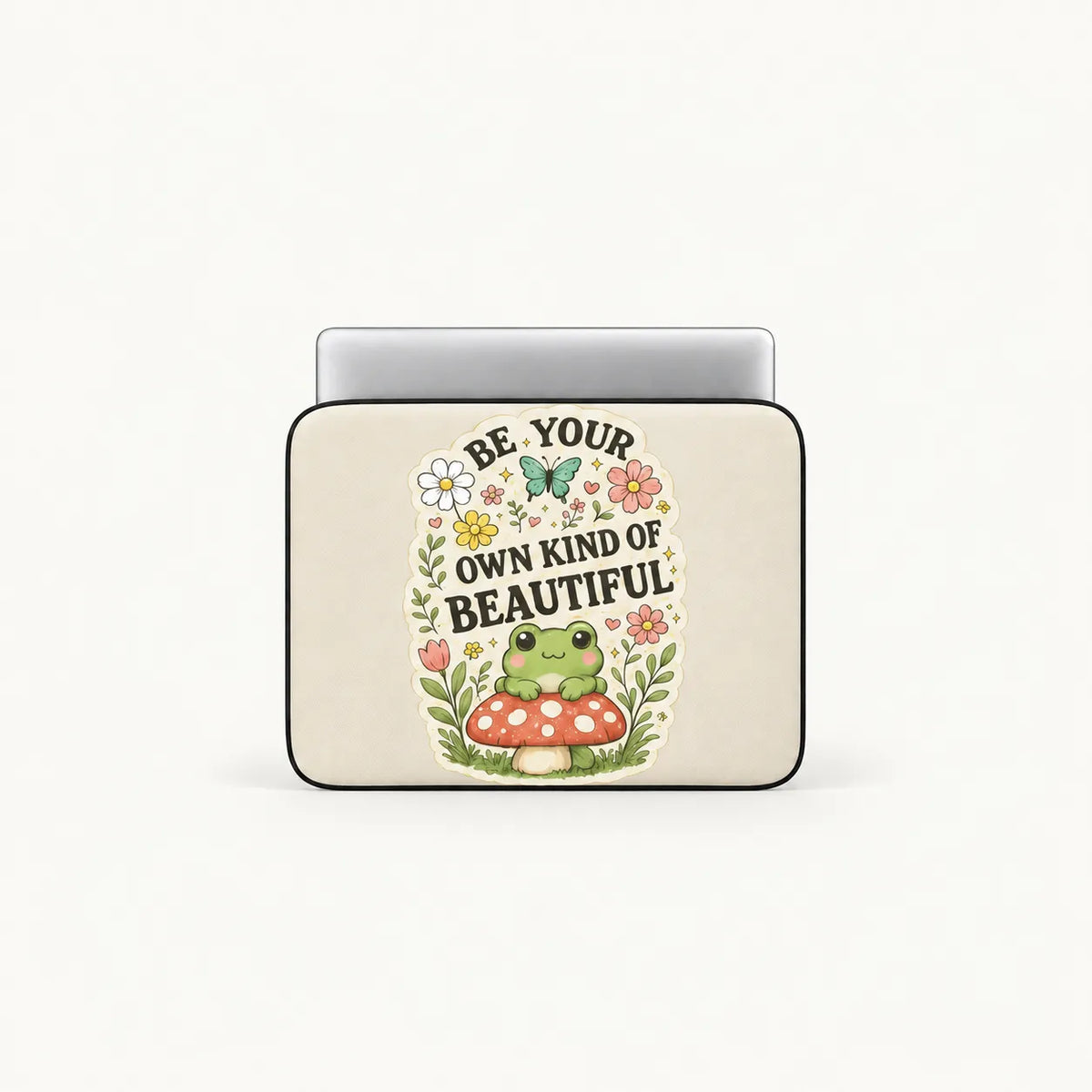 Cute green frog sitting on a red toadstool surrounded by flowers and Be Your Own Kind of Beautiful typography on cream padded laptop sleeve by SLEEVER
