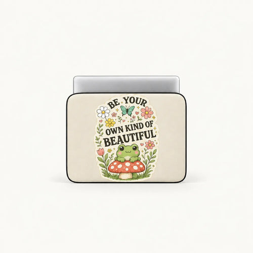 Cute green frog sitting on a red toadstool surrounded by flowers and Be Your Own Kind of Beautiful typography on cream padded laptop sleeve by SLEEVER