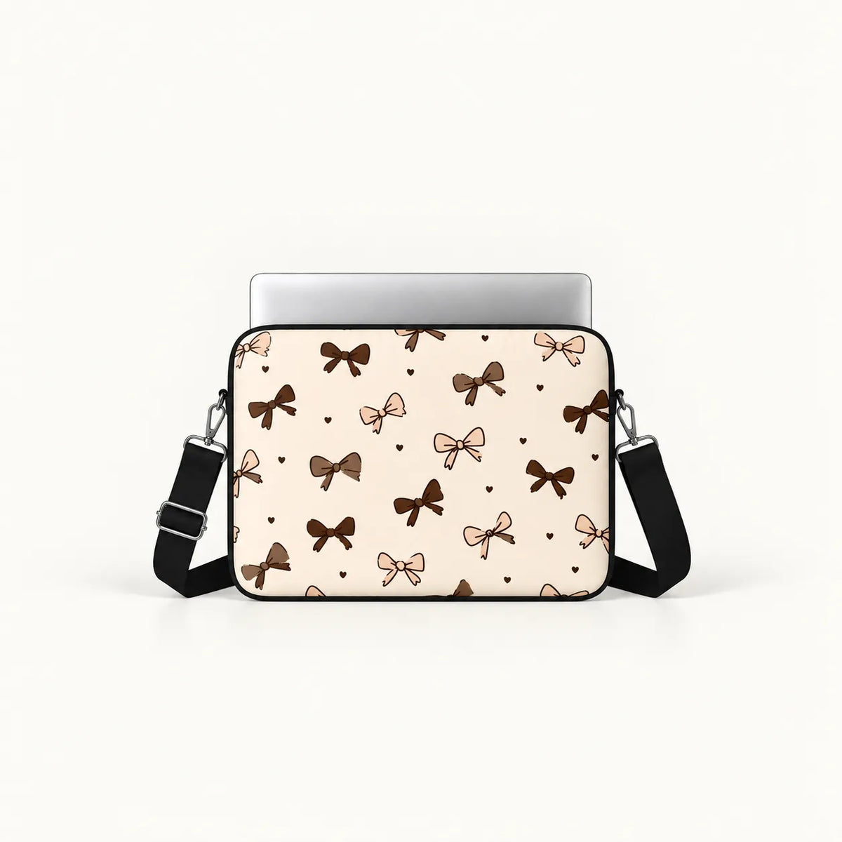 A beige laptop sleeve with a repeating pattern of brown and pink bows and small hearts, featuring a black adjustable shoulder strap and a silver laptop inserted at the top, shown on a clean white background.