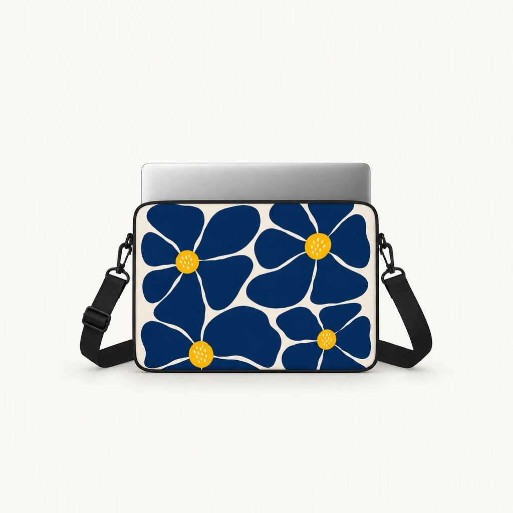 A laptop sleeve featuring a bold navy blue and white floral pattern with yellow centers, shown with a silver laptop inside and a black shoulder strap on a light gray background.
