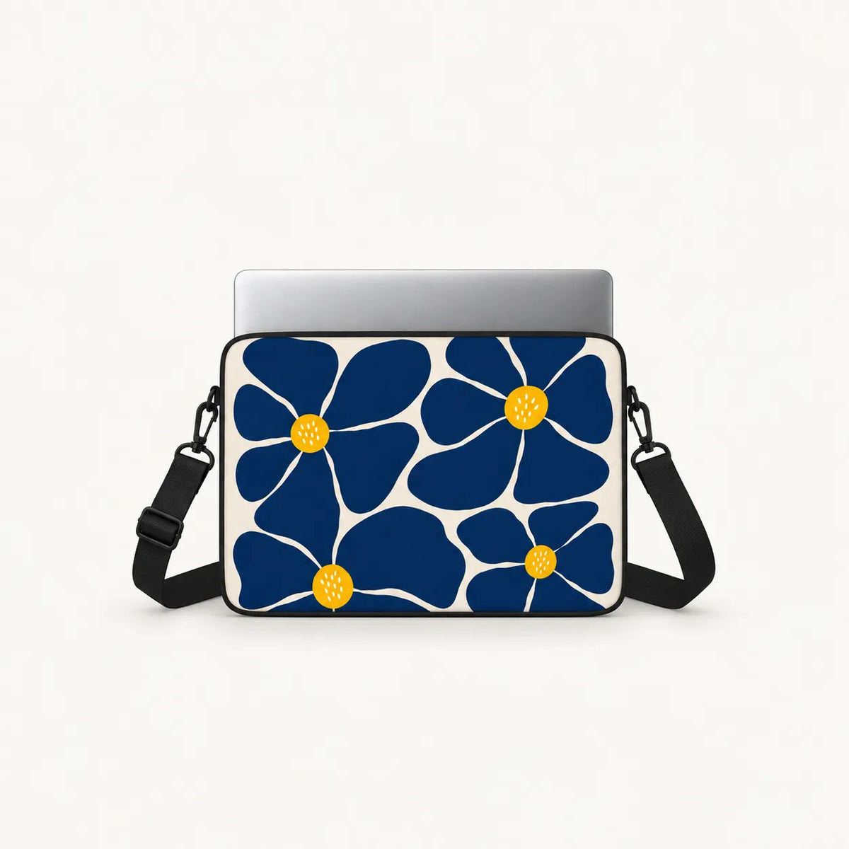 A laptop sleeve featuring a bold navy blue and white floral pattern with yellow centers, shown with a silver laptop inside and a black shoulder strap on a light gray background.