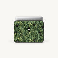 A laptop sleeve featuring a green and black leafy pattern with small peeking black cats, shown on a silver laptop against a light gray background.