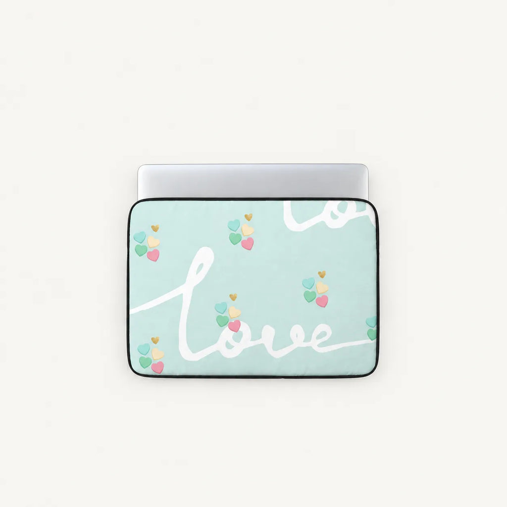A laptop sleeve with a light mint green background, featuring the word 'love' in white cursive script and small colorful heart balloons. The sleeve is shown with a silver laptop inserted, set against a plain off-white background.