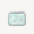 A laptop sleeve with a light mint green background, featuring the word 'love' in white cursive script and small colorful heart balloons. The sleeve is shown with a silver laptop inserted, set against a plain off-white background.