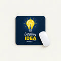 A square dark navy mouse pad with a yellow lightbulb graphic and the text 'Everything BEGINS WITH AN IDEA' in white and yellow, shown on a light beige background with a white computer mouse resting on it.